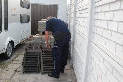 policjant liczący kratki zabezpieczające studzienki kanalizacyjne