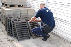 policjant liczący kratki zabezpieczające studzienki kanalizacyjne