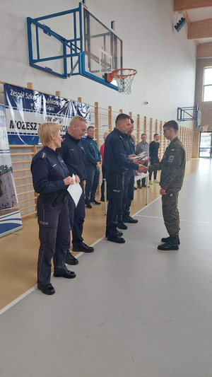 Komendant w asyście policjantów wręcza dyplom  zastępcy zwycięzcy konkursu